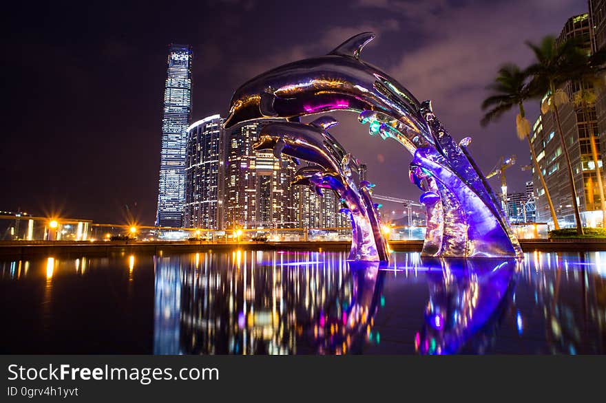 A fountain with a dolphin sculpture in a city at night. A fountain with a dolphin sculpture in a city at night.