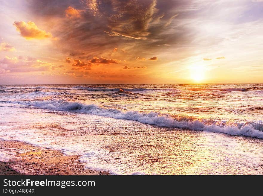 Golden sunset breaking through cloud remnants and with waves breaking onto a shingle beach. Golden sunset breaking through cloud remnants and with waves breaking onto a shingle beach.