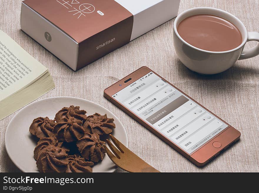 A chocolate color smartphone with a plate of chocolates and a cup of hot chocolate. A chocolate color smartphone with a plate of chocolates and a cup of hot chocolate.