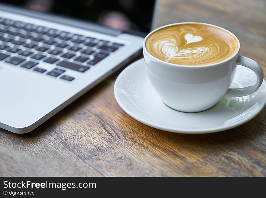 A laptop computer next to a cup of cappuccino on a table. A laptop computer next to a cup of cappuccino on a table.