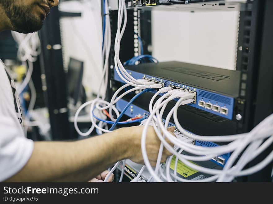 A man installing cables on a router or switch in a server rack. A man installing cables on a router or switch in a server rack.