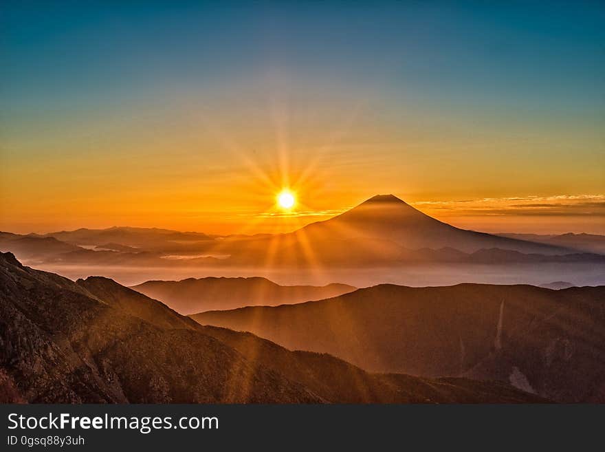 Sunset over mountain valley with volcano against blue skies.