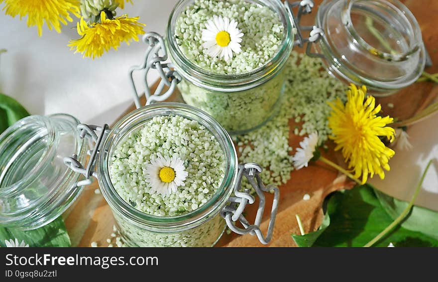 Green herbal aromatherapy salts in glass jars with flowers.