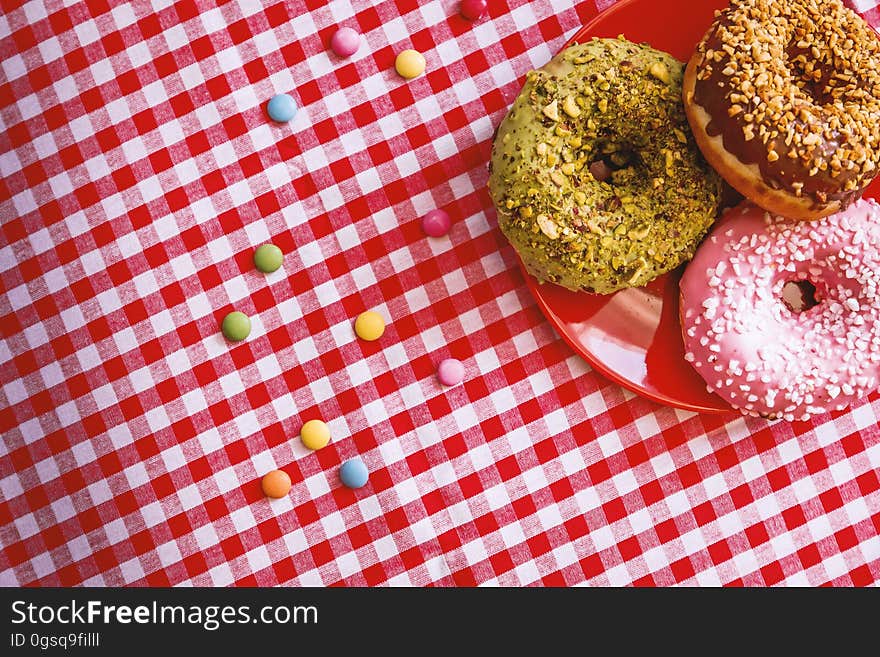 Overhead of frosted donuts on red plate on checked tablecloth. Overhead of frosted donuts on red plate on checked tablecloth.