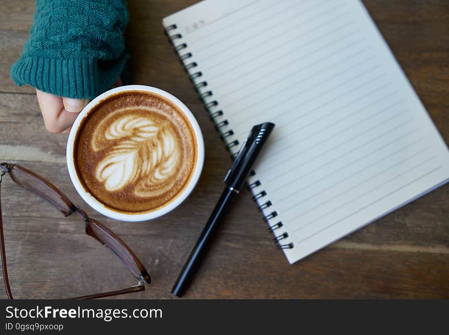 Hand holding cup of coffee next to blank open notebook and pen with eyeglasses. Hand holding cup of coffee next to blank open notebook and pen with eyeglasses.