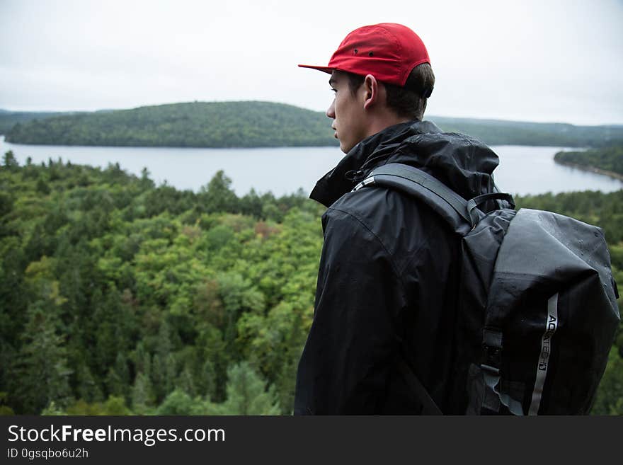 Man standing on hilltop with backpack overlooking forest along banks of lake. Man standing on hilltop with backpack overlooking forest along banks of lake.