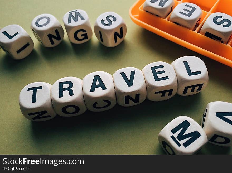 Upper case black letters on small white cubes with one complete meaningful word spelling "travel", green background.