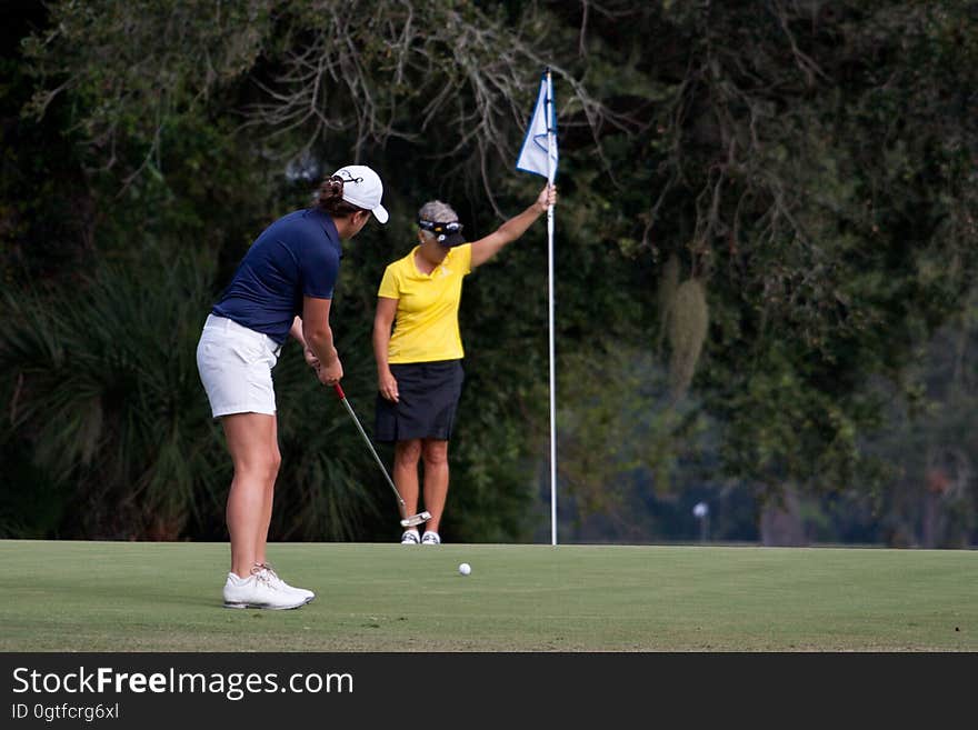 A golfer tries to get her ball into the hole while her partner looks on. A golfer tries to get her ball into the hole while her partner looks on.