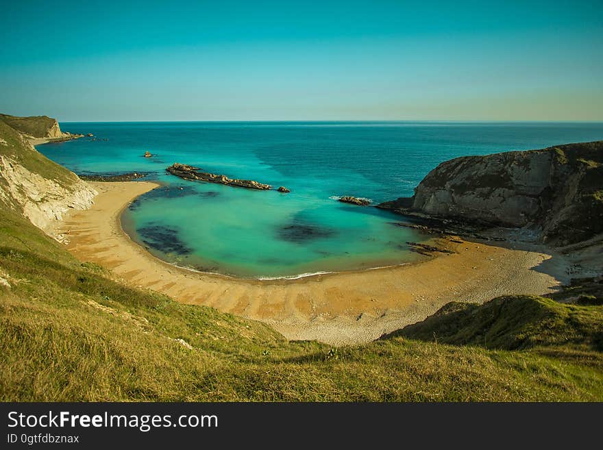 Sheltered beach on the sunny shore of an aquamarine sea with blue cloudless sky. Sheltered beach on the sunny shore of an aquamarine sea with blue cloudless sky.