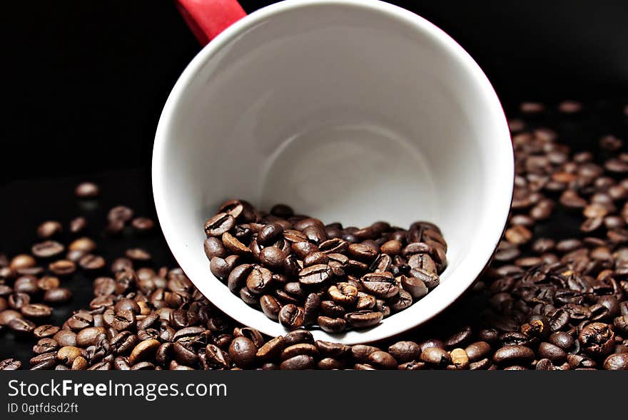 Coffee beans in and surrounding a coffee cup.