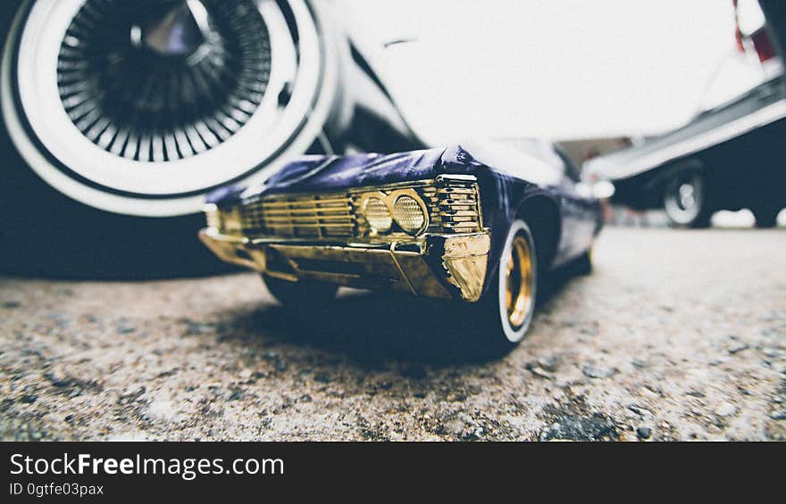 A close up of a classic toy car on a street with real cars. A close up of a classic toy car on a street with real cars.