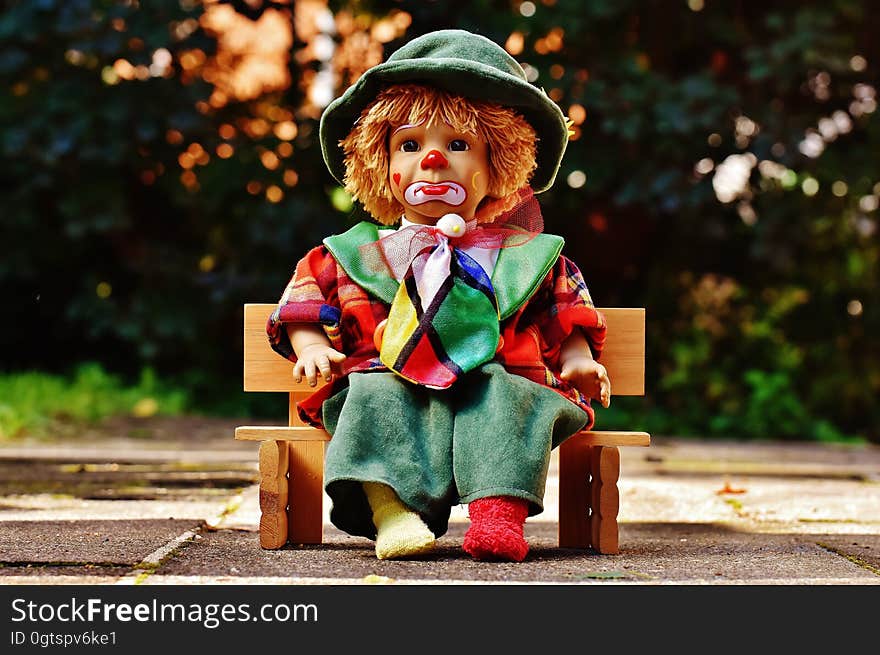 Clown doll with sad expression on wooden bench outdoors. Clown doll with sad expression on wooden bench outdoors.