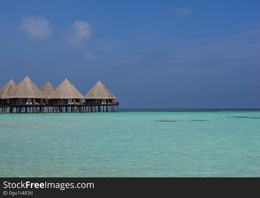 Resort bungalows in Maldives on wooden stilts over clear blue water against blue sunny skies. Resort bungalows in Maldives on wooden stilts over clear blue water against blue sunny skies.