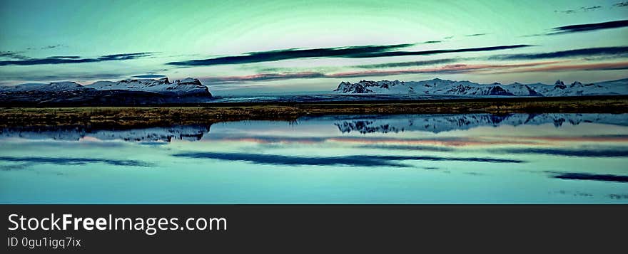 Panorama of mountains along coastline with green skies reflecting in calm waters. Panorama of mountains along coastline with green skies reflecting in calm waters.