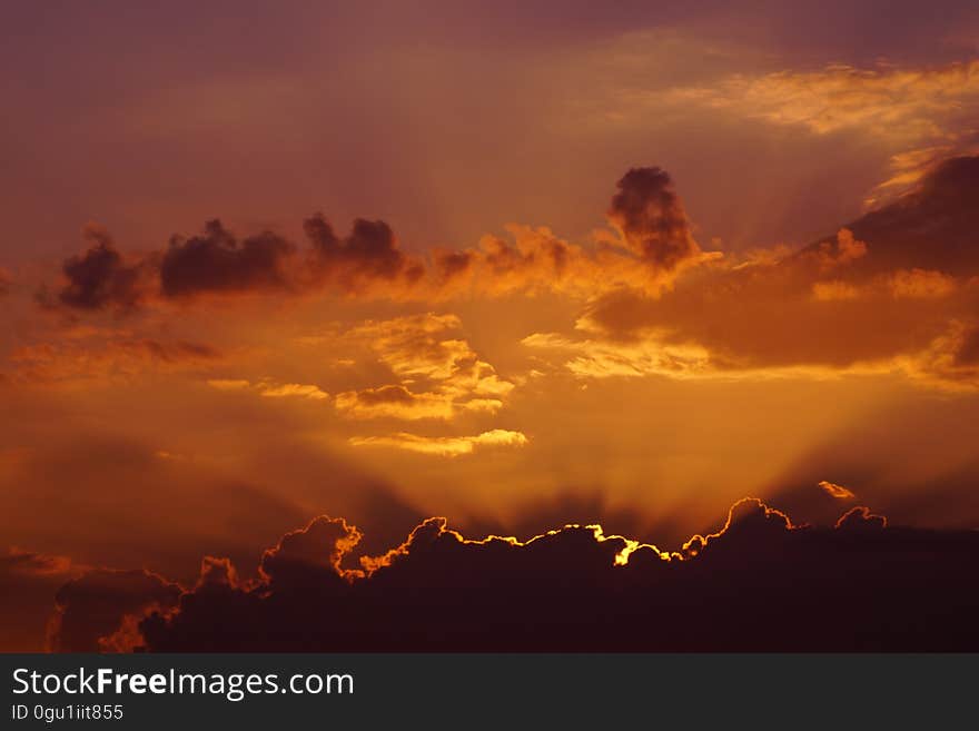 Orange skies at sunset behind clouds in sky.