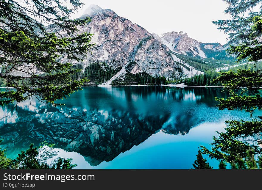 Mountain peaks reflecting in blue waters of alpine lake with green pine trees on sunny day. Mountain peaks reflecting in blue waters of alpine lake with green pine trees on sunny day.