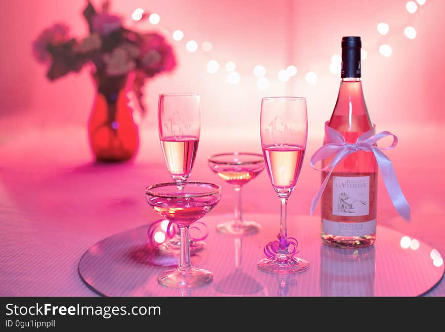 A bottle of rose wine or champagne with glasses on a table in red color. A bottle of rose wine or champagne with glasses on a table in red color.