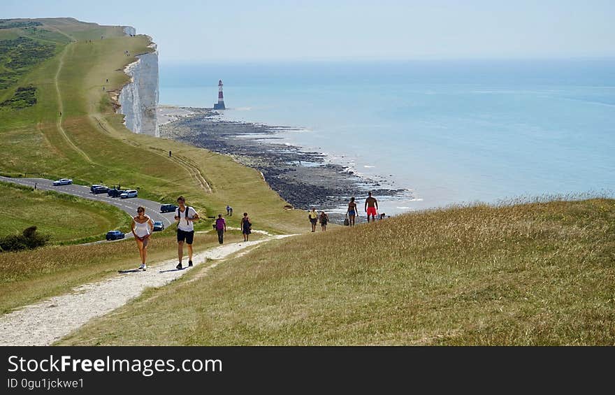 People walking at the White Cliffs of Dover at the Strait of Dover with a lighthouse in the distance.