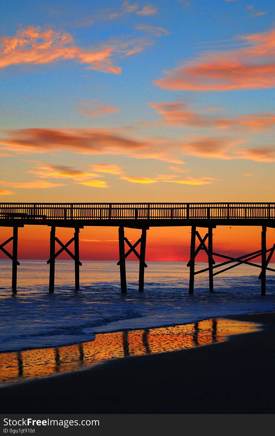 Dramatic orange sunset behind a bridge or pier with safety rails supported on stilts above the sea. Dramatic orange sunset behind a bridge or pier with safety rails supported on stilts above the sea.