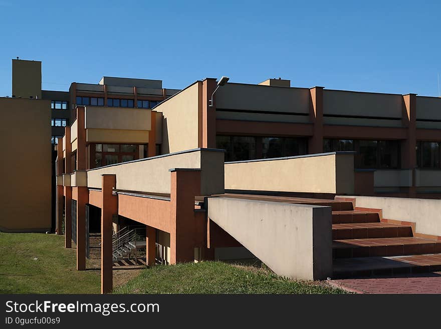 Entrance stairs and open air bridge leading to low rise modern buildings such as a university or hospital, blue sky background. Entrance stairs and open air bridge leading to low rise modern buildings such as a university or hospital, blue sky background.