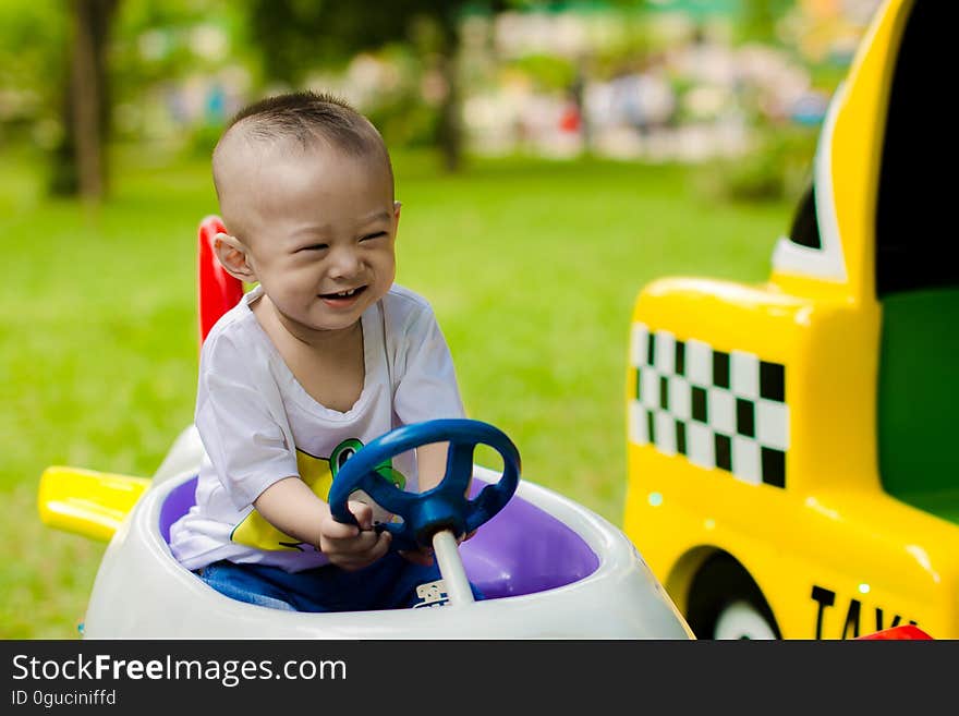 Happy smiling baby boy in white t-shirt driving toy car in the garden with yellow taxi alongside. Happy smiling baby boy in white t-shirt driving toy car in the garden with yellow taxi alongside.