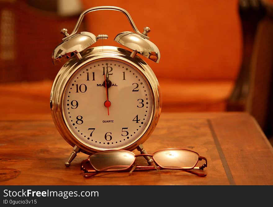 A classic alarm clock and eyeglasses on table.