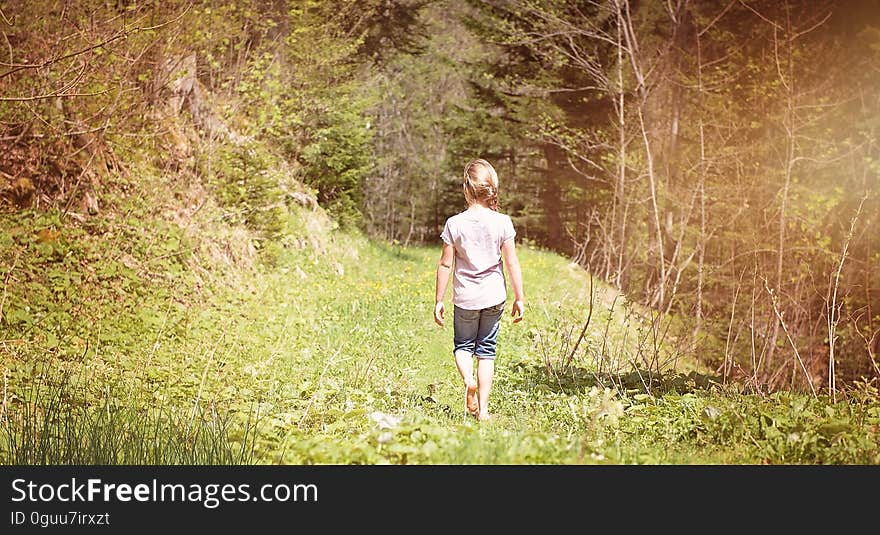 Young blond girl walking alone through a green landscape with grasses, ferns, bushes and trees. Young blond girl walking alone through a green landscape with grasses, ferns, bushes and trees.