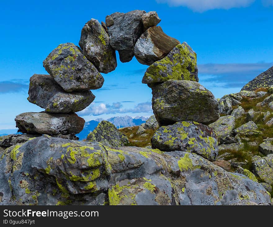 Strange semicircle of boulders partly covered in green moss on a rocky mountain top with a view through them to the distant horizon, blue almost cloudless sky. Strange semicircle of boulders partly covered in green moss on a rocky mountain top with a view through them to the distant horizon, blue almost cloudless sky.