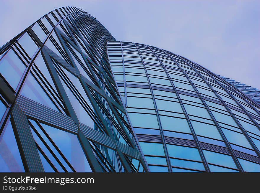 Curved architectural facade of high rise buildings constructed of glass, steel and concrete, pale blue sky reflected in the glass. Curved architectural facade of high rise buildings constructed of glass, steel and concrete, pale blue sky reflected in the glass.