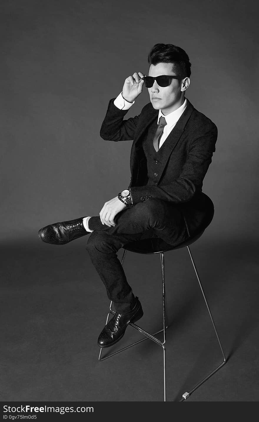 A man wearing suit and sunglasses sitting on chair in black and white. A man wearing suit and sunglasses sitting on chair in black and white.