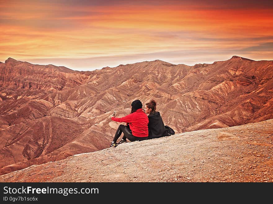 2 Woman Seating on the Mountain Cliff during Golden Hour