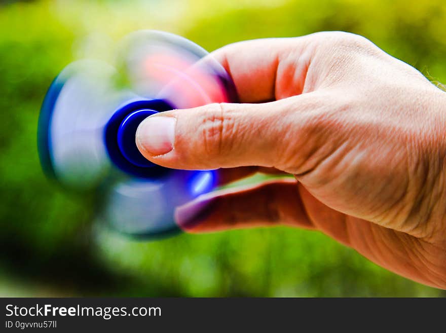 Hand of man using fidget spinner outdoors with green nature background.