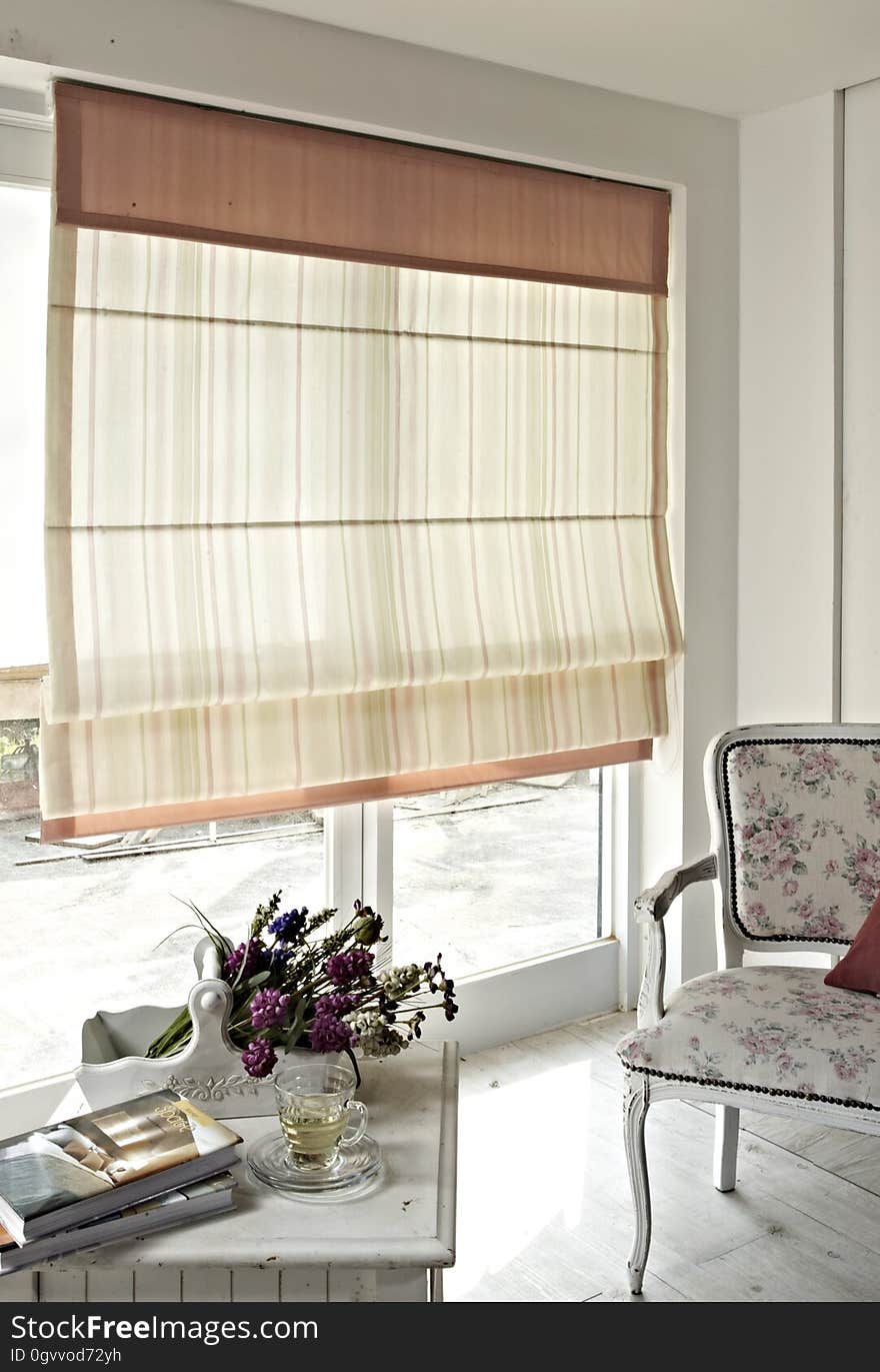 Luxurious modern living room with table and chair by large window with partially pulled blinds.