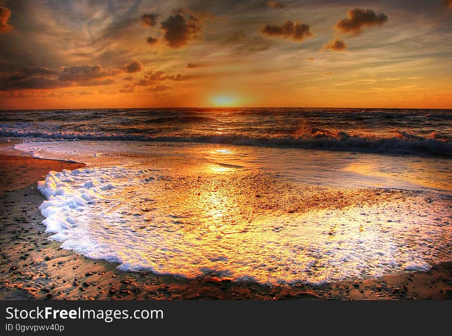 Beautiful golden sunset with incoming tide producing gold tinged white foam over a sandy beach. Beautiful golden sunset with incoming tide producing gold tinged white foam over a sandy beach.