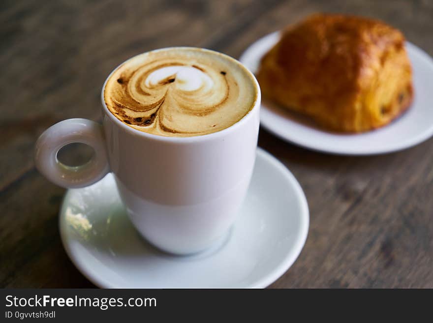 Breakfast cappuccino and bun on wooden table.