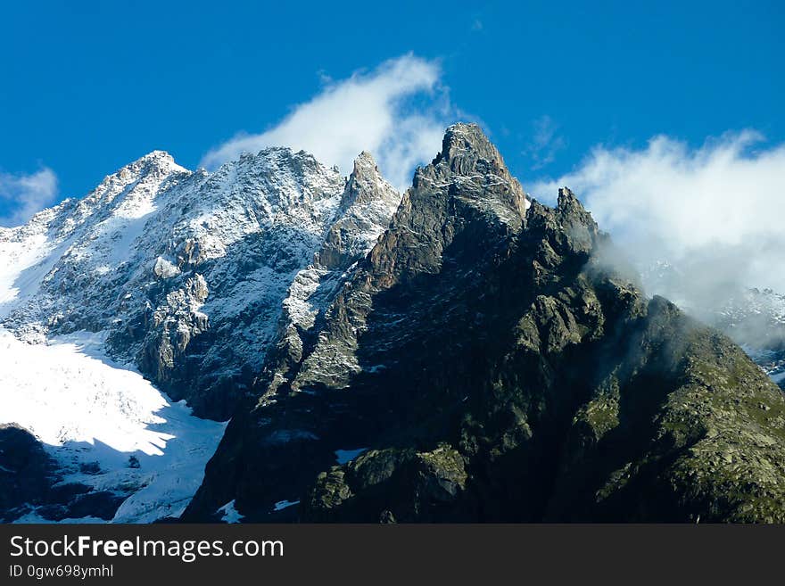 Snow covered mountain peaks with clouds against blue skies on sunny day. Snow covered mountain peaks with clouds against blue skies on sunny day.