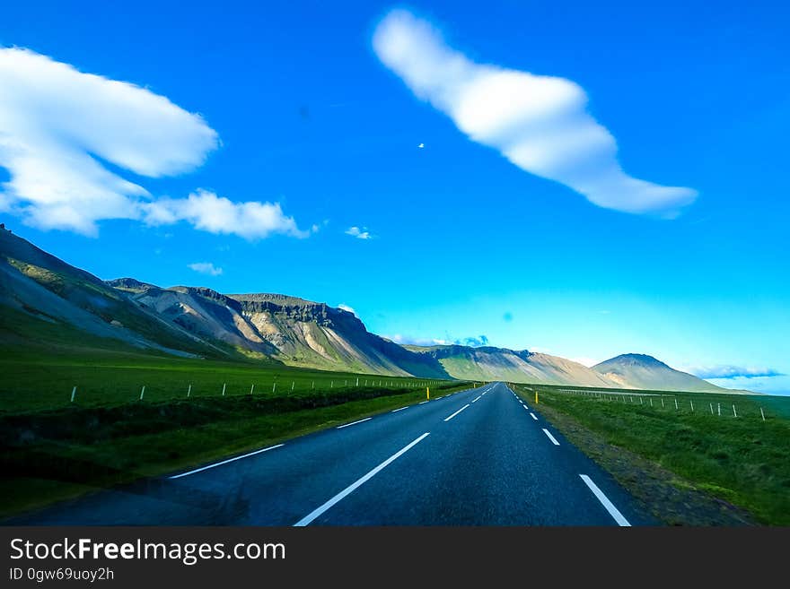 Empty country road through green fields surrounded with hills. Empty country road through green fields surrounded with hills.