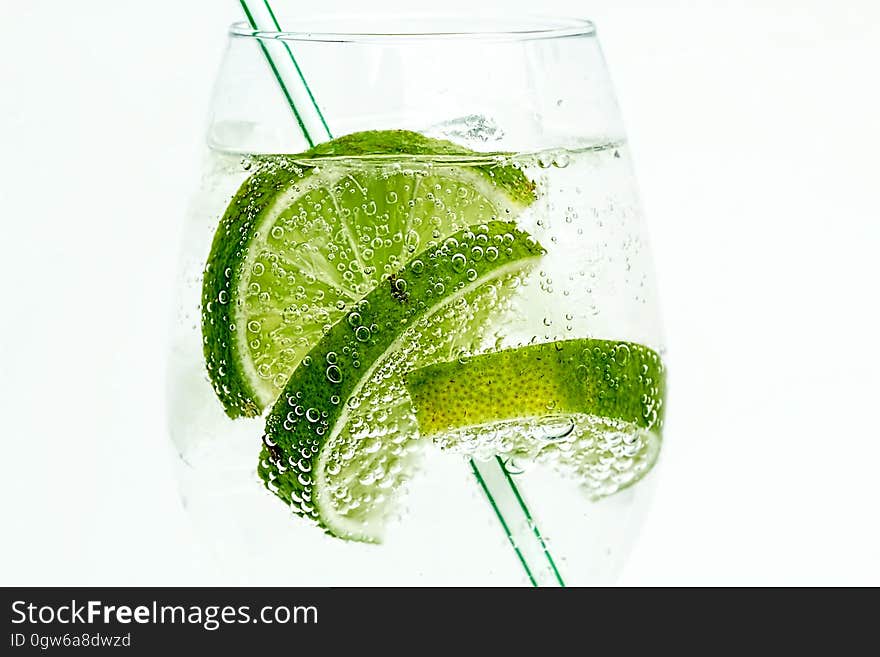 Drinking glass with clear carbonated beverage with line wedges and straw on white. Drinking glass with clear carbonated beverage with line wedges and straw on white.