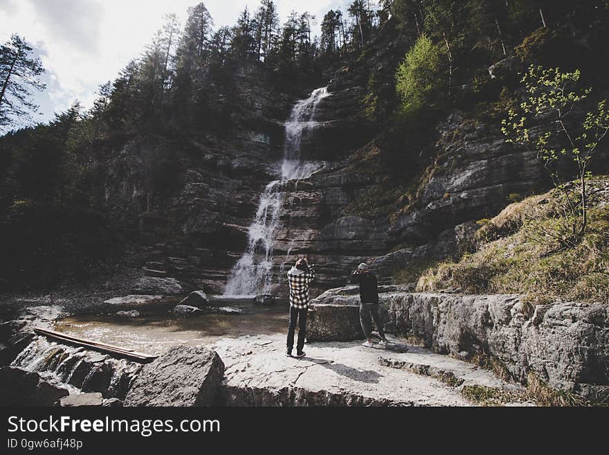 Hikers standing next to waterfall along hillside in forest. Hikers standing next to waterfall along hillside in forest.