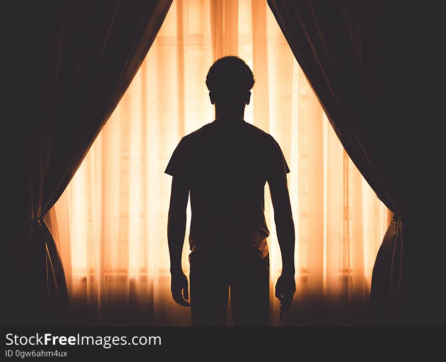 Silhouette of young boy standing in front of curtains on interior window. Silhouette of young boy standing in front of curtains on interior window.