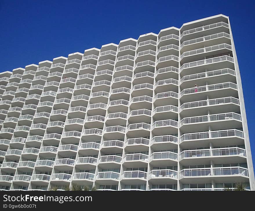 Balconies on exterior of modern apartment building against blue skies on sunny day.