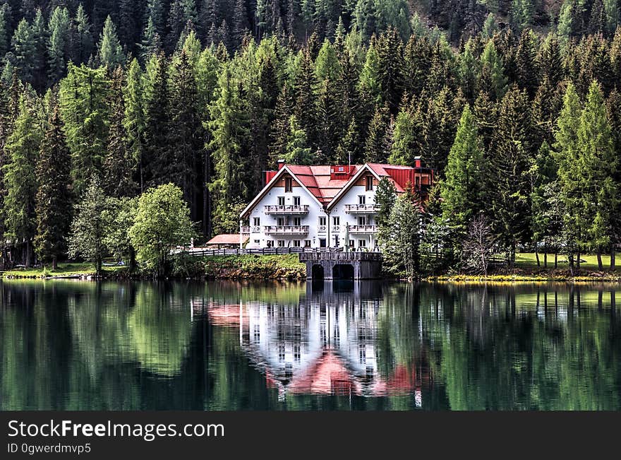 A chalet on the lake coast reflecting on the water surface and an evergreen forest in the background. A chalet on the lake coast reflecting on the water surface and an evergreen forest in the background.