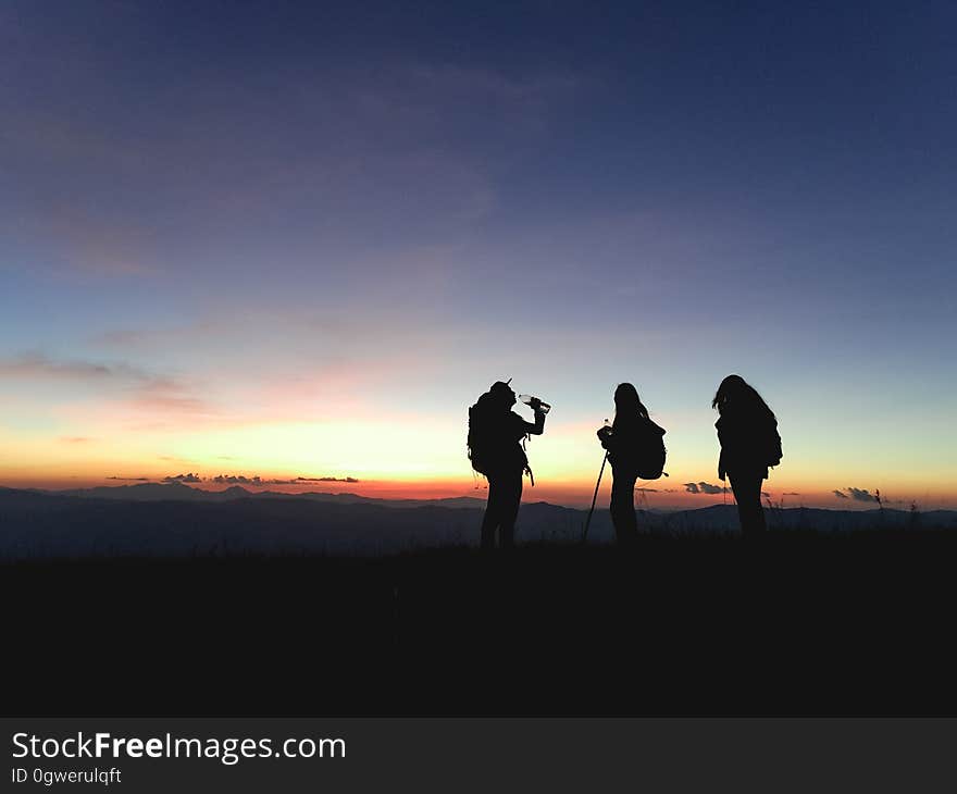 The silhouettes of three people standing on a mountain at sunset. The silhouettes of three people standing on a mountain at sunset.