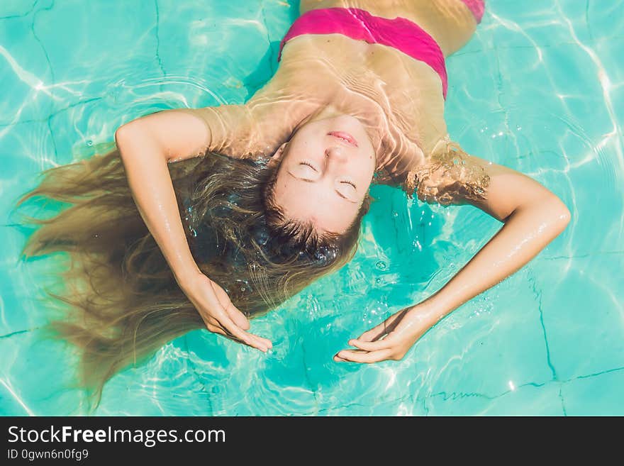 Beautiful young woman floating in pool relaxing Top view. Holiday concept.