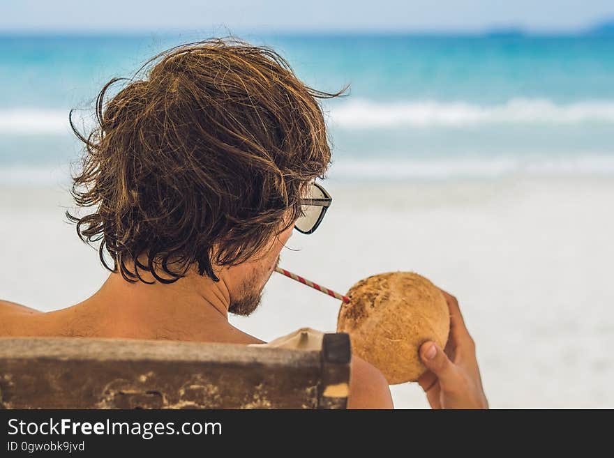 Young man drinking coconut milk on Chaise-longue on beach.