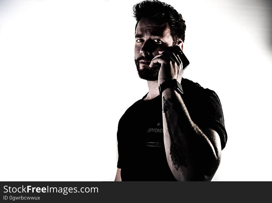 Dark bearded man with shock of black hair, black jumper and tattoo using mobile phone and looking distressed or disturbed by the message, white background. Dark bearded man with shock of black hair, black jumper and tattoo using mobile phone and looking distressed or disturbed by the message, white background.