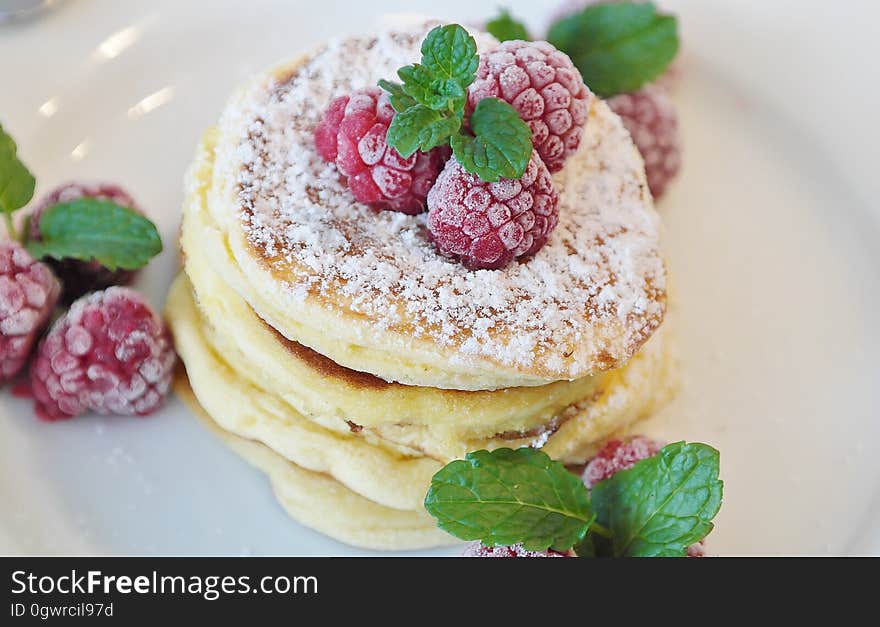 A plate of pancakes with raspberries and mint leaves on top. A plate of pancakes with raspberries and mint leaves on top.