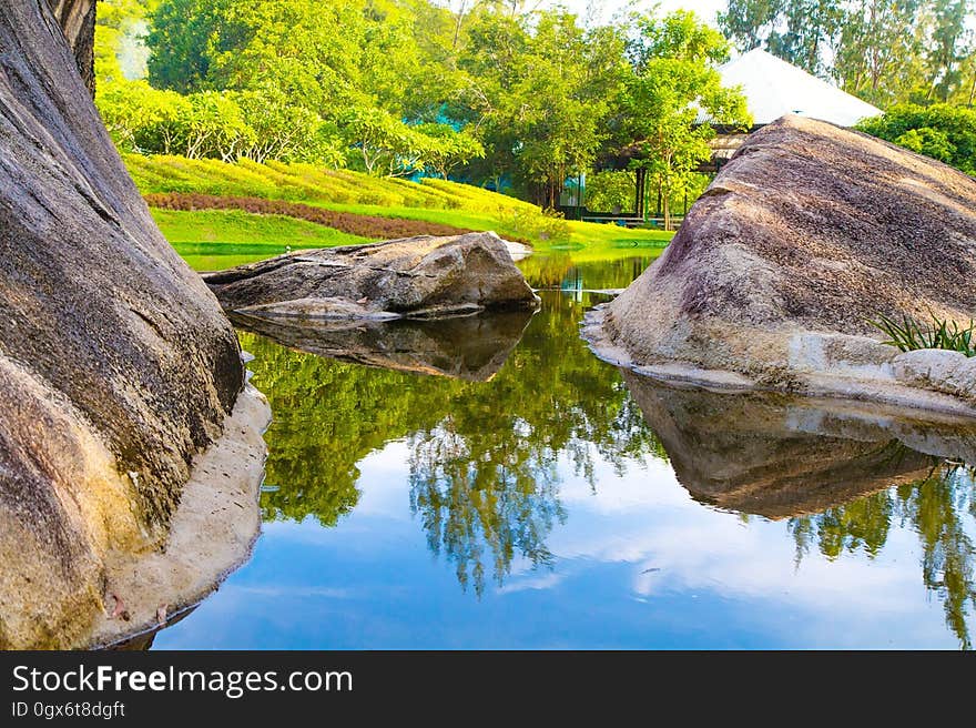 Scenic view of green trees and large boulders reflecting on lake in park, summer scene. Scenic view of green trees and large boulders reflecting on lake in park, summer scene.