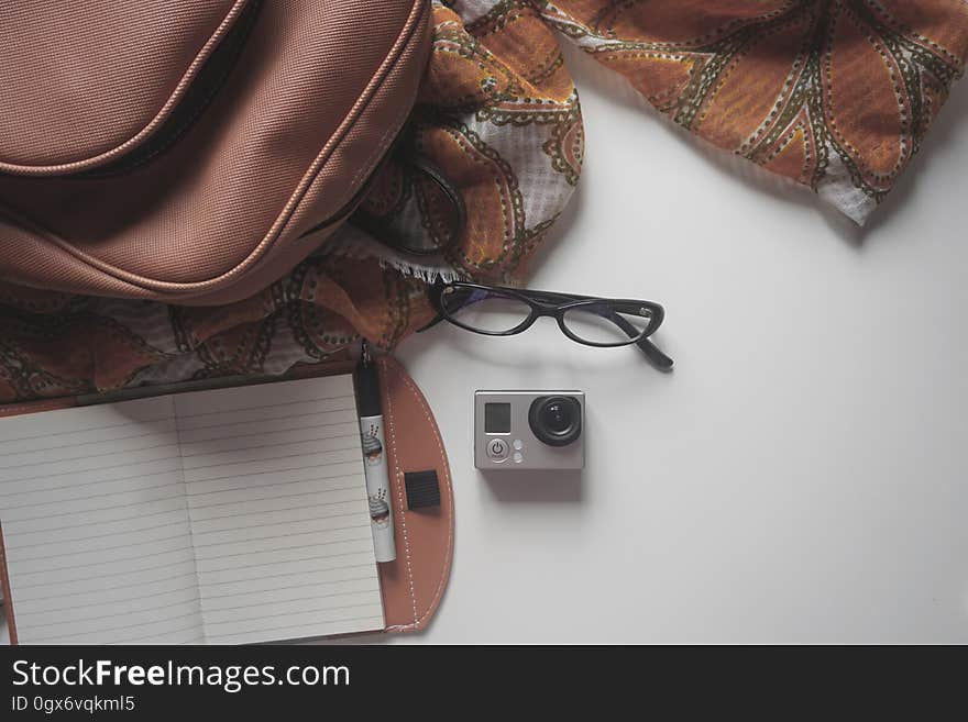 Black Eyeglasses on Top of the Gray and Black Action Camera in the White Surface