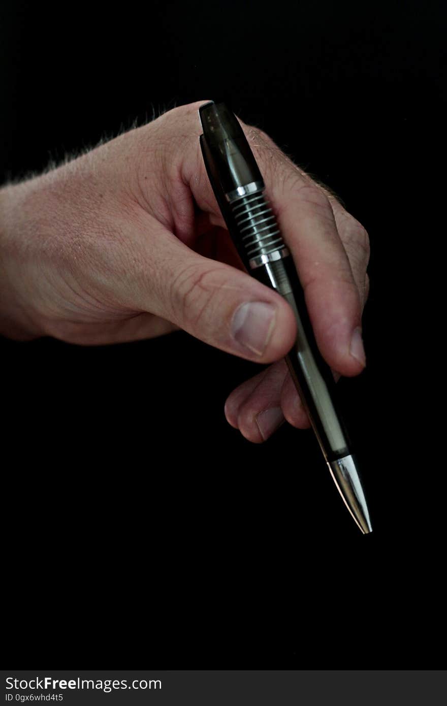 Close up of hand holding black pen against black background. Close up of hand holding black pen against black background.